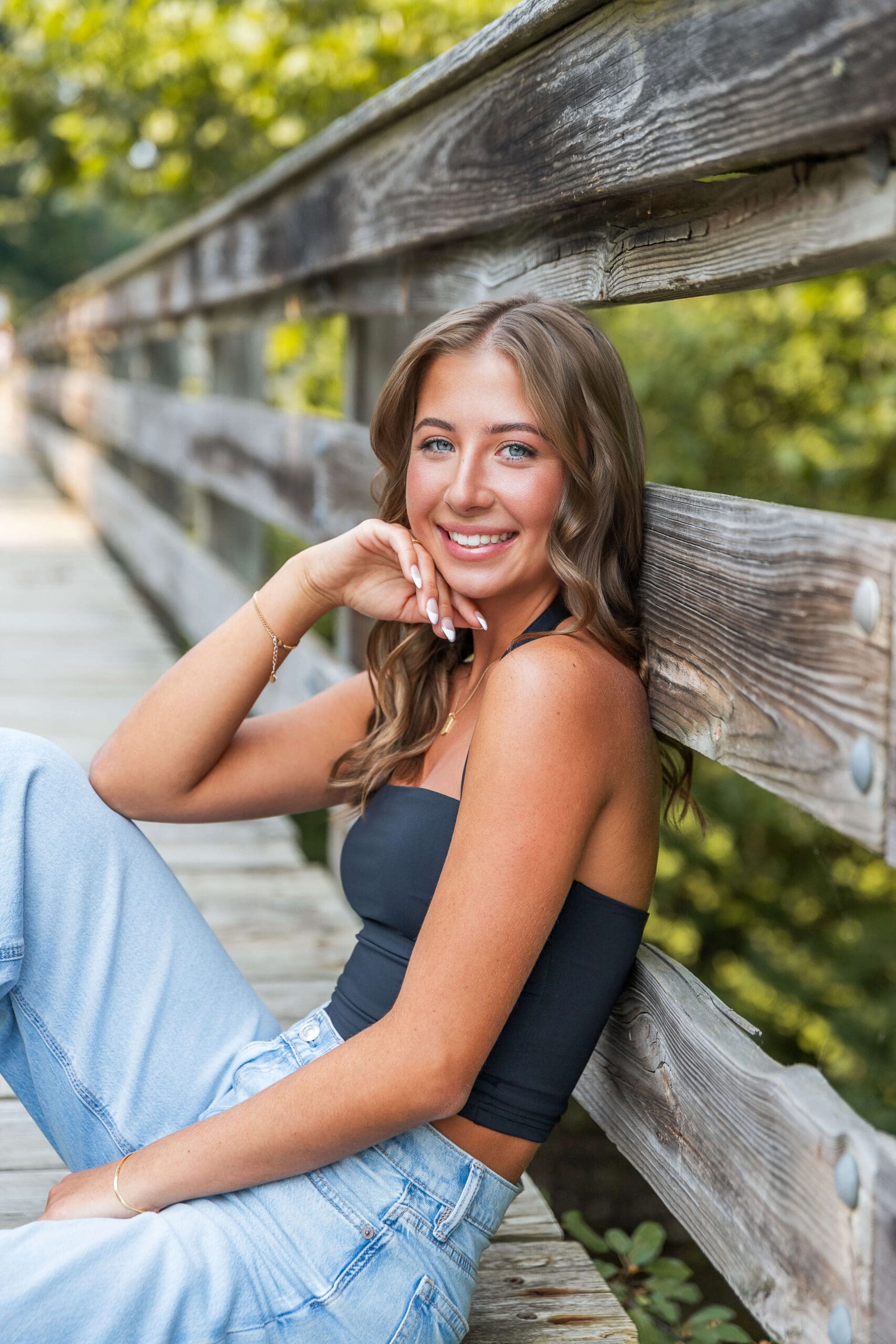 A smiling high school senior leans against a wooden boardwalk railing in a park