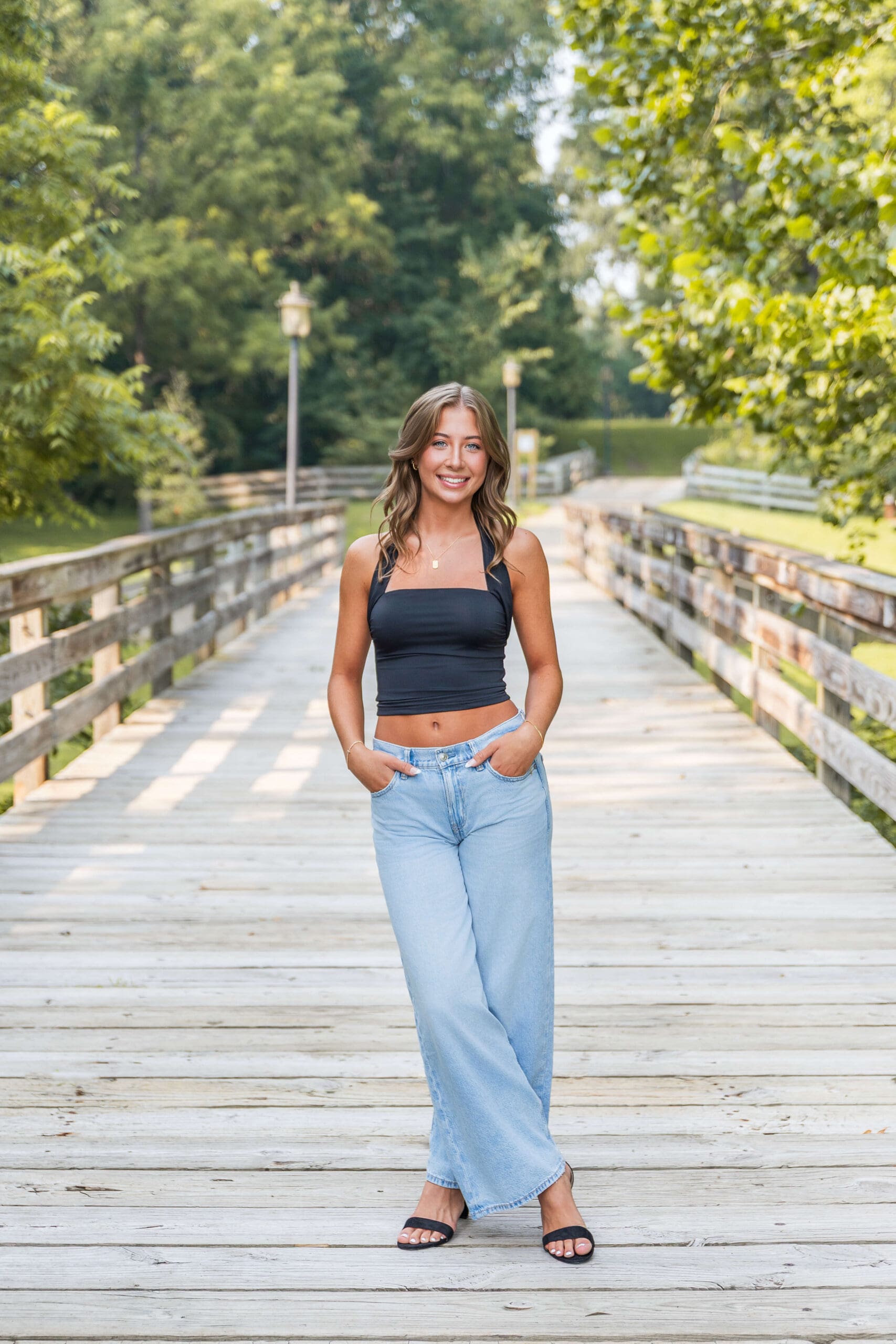 A high school senior stands in a boardwalk smiling in a black blouse and jeans after visiting nail salons in metro detroit