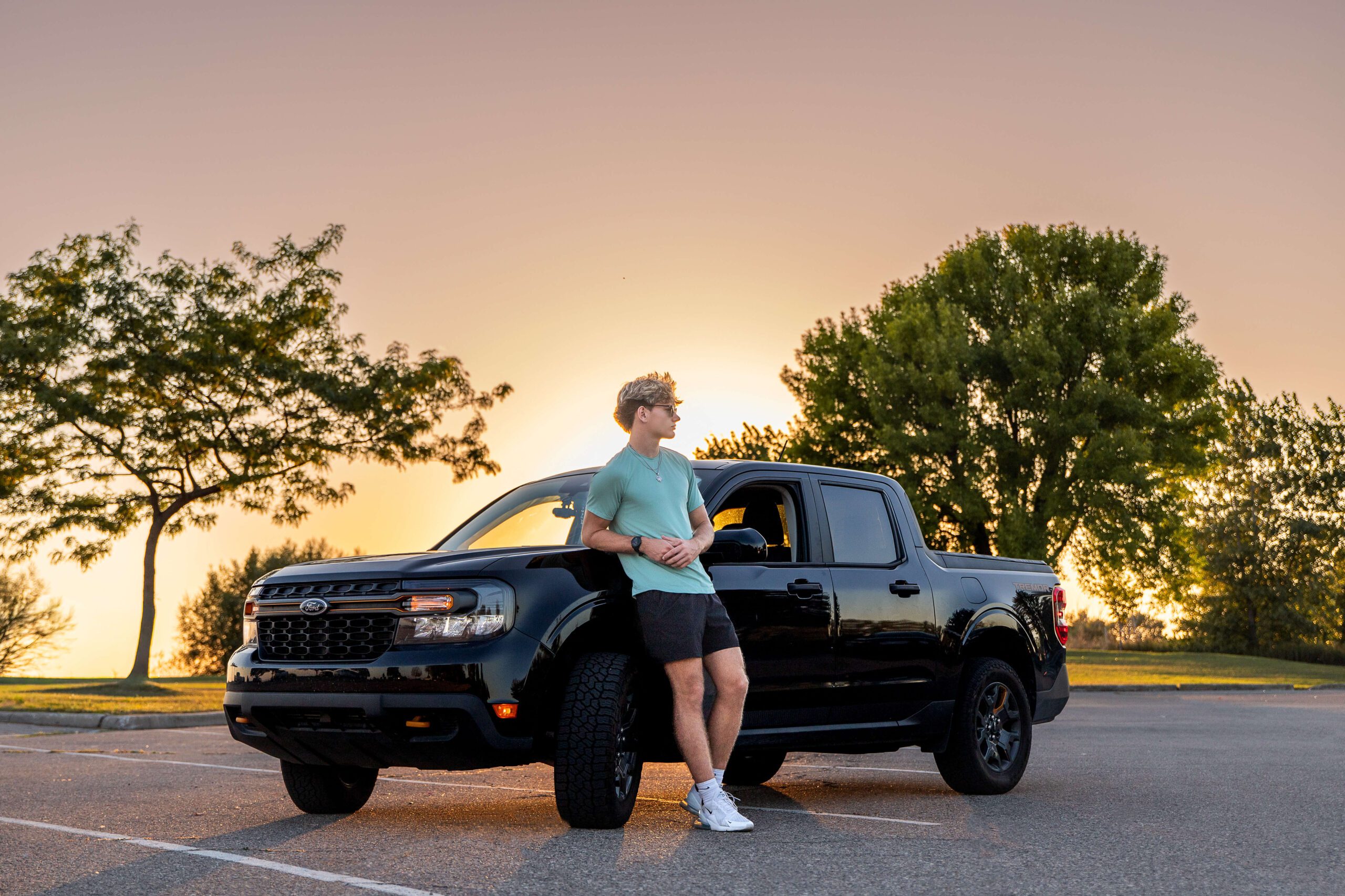 A man leaning on a ford truck in a parking lot at sunset