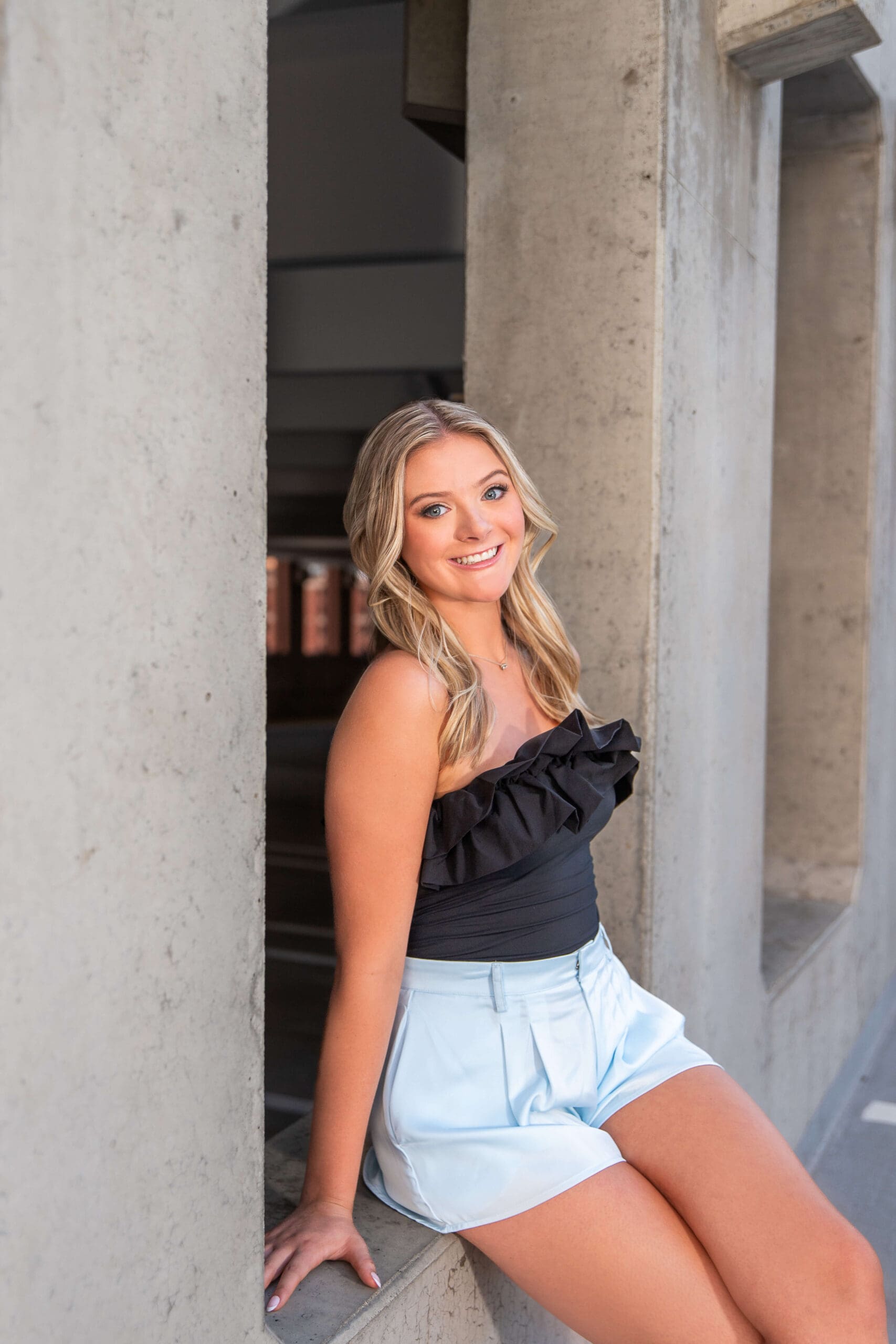 A happy graduate sits in a concrete window in a black blouse