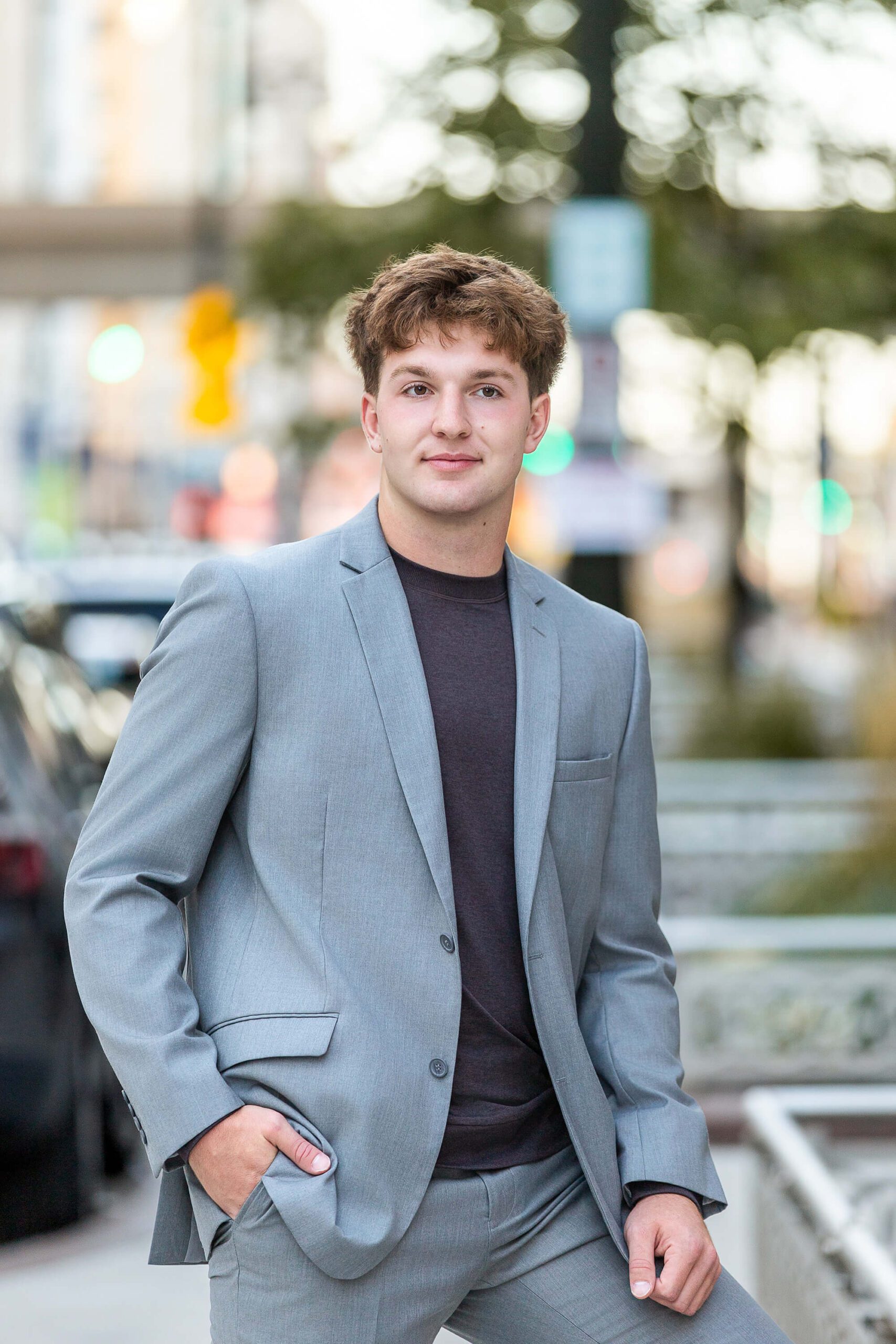 A teenage boy in a grey suit stands in a park after finding great tux rental in detroit