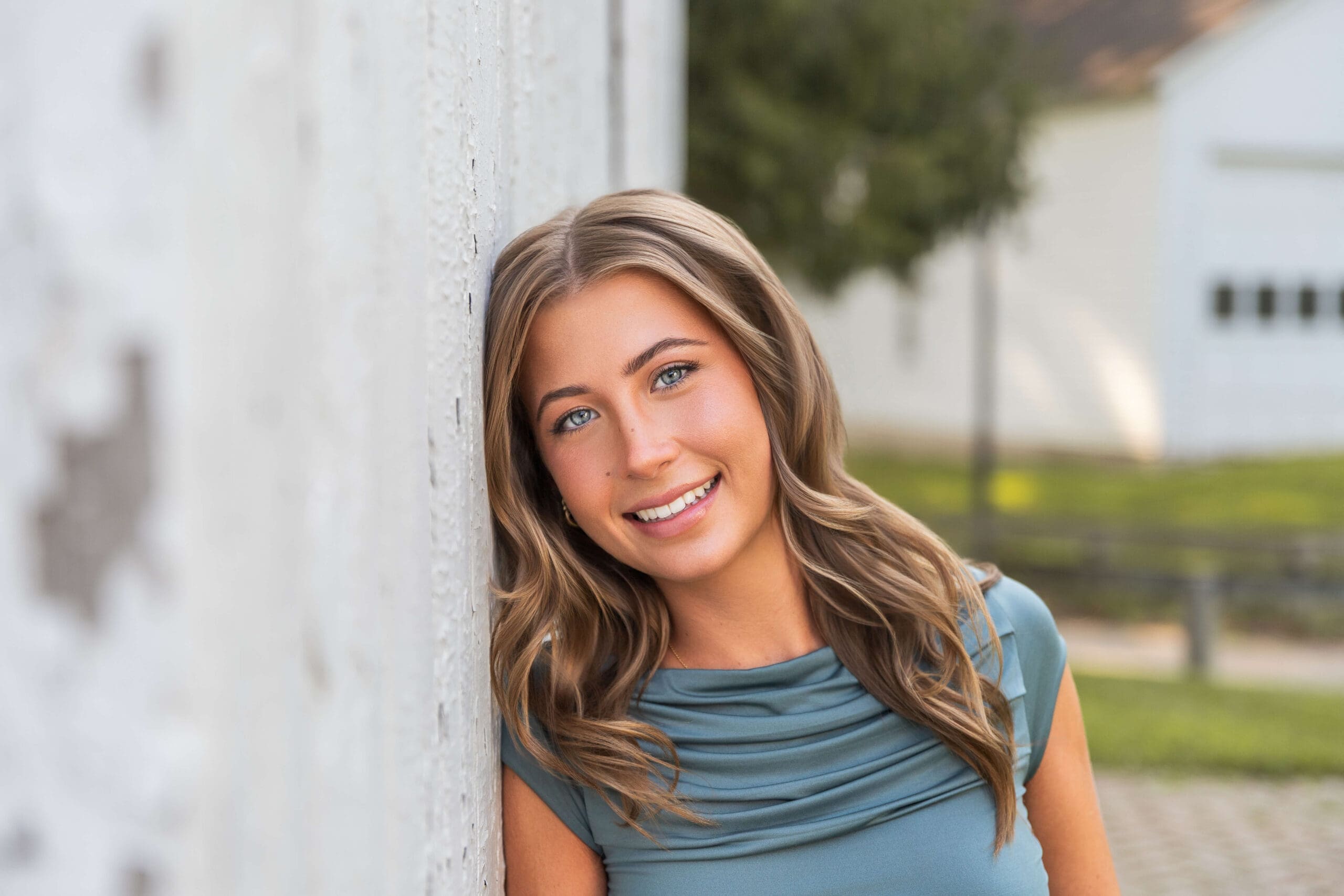 A closeup of a high school senior leaning on a white rustic building