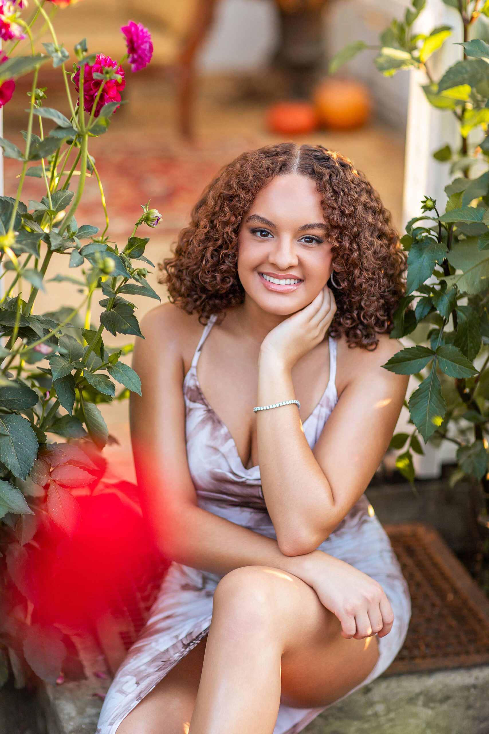 A high school senior sits on a garden bench smiling in a light gown surrounded by roses after finding hair salons in washington mi