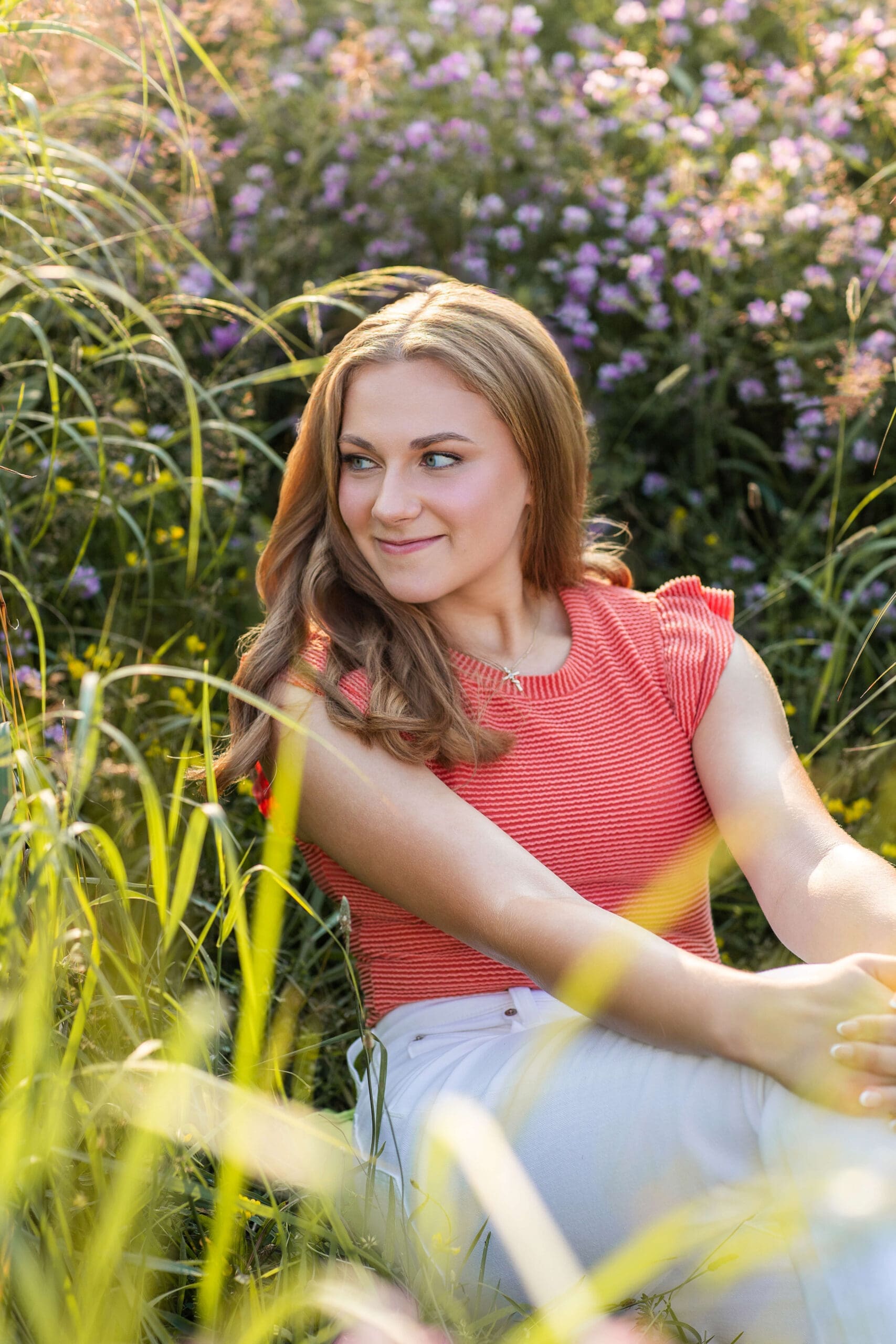 A graduate in a pink blouse sits in a field of wildflowers smiling at sunset after earning scholarships for detroit students