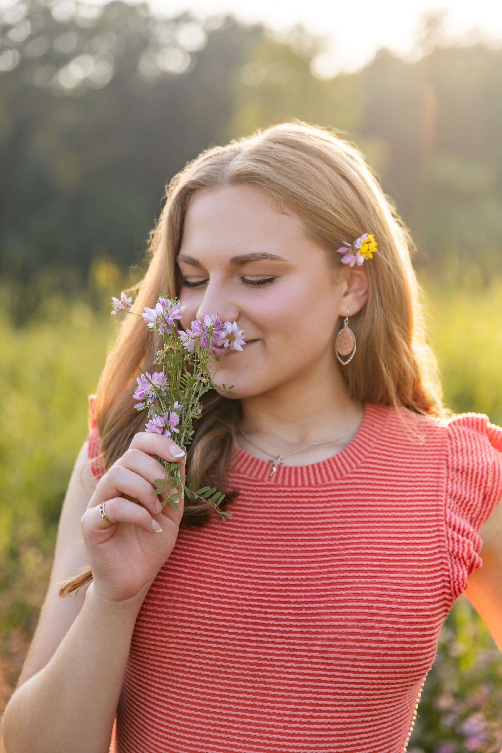 A high school senior in a pink blouse smells purple flowers in a field at sunset after finding scholarships for detroit students