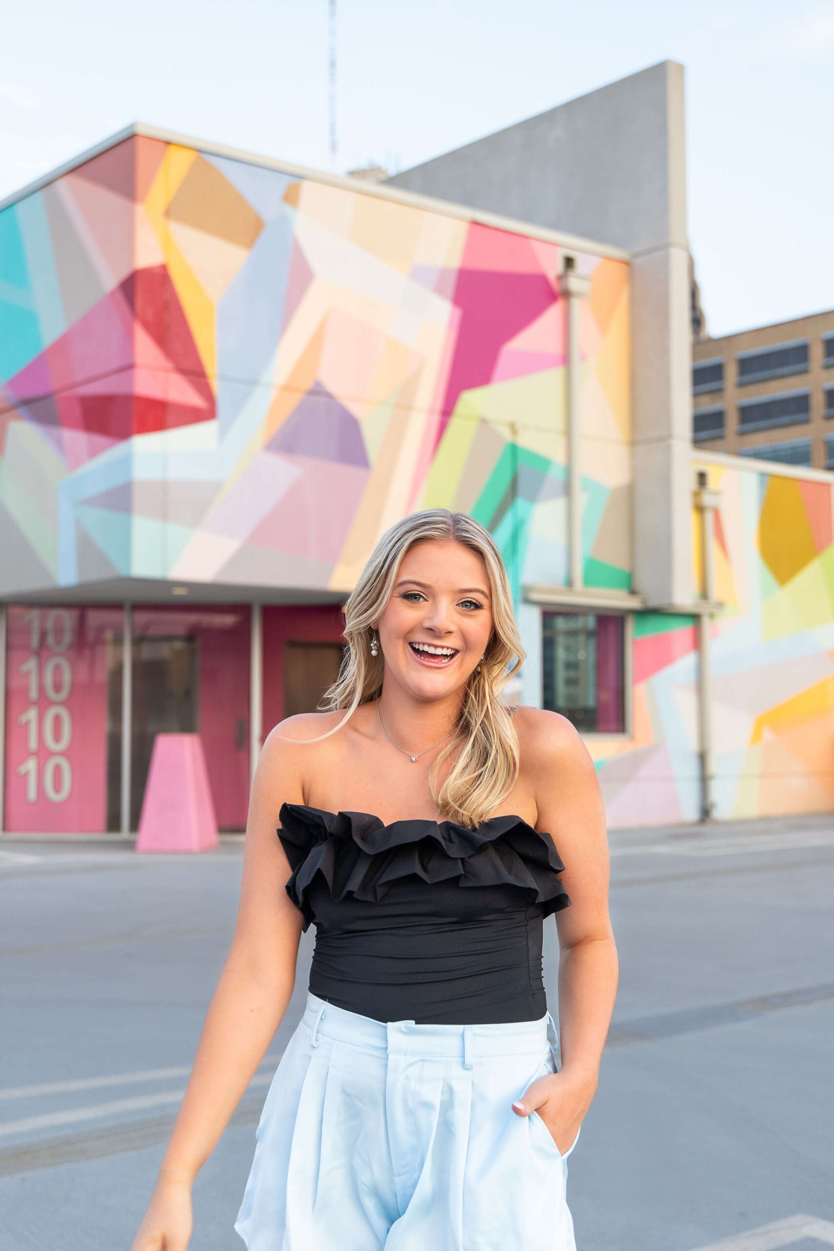 A happy high school grad in a black blouse smiles in front of a colorful building during things to do with teens in detroit